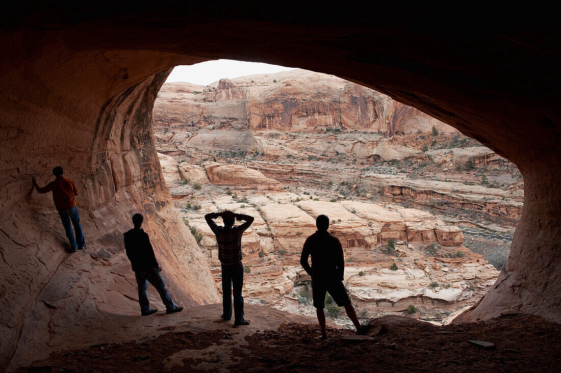 Four young men are silloutted against the mouth of a cave in Moab, UT Moab, Utah, USA