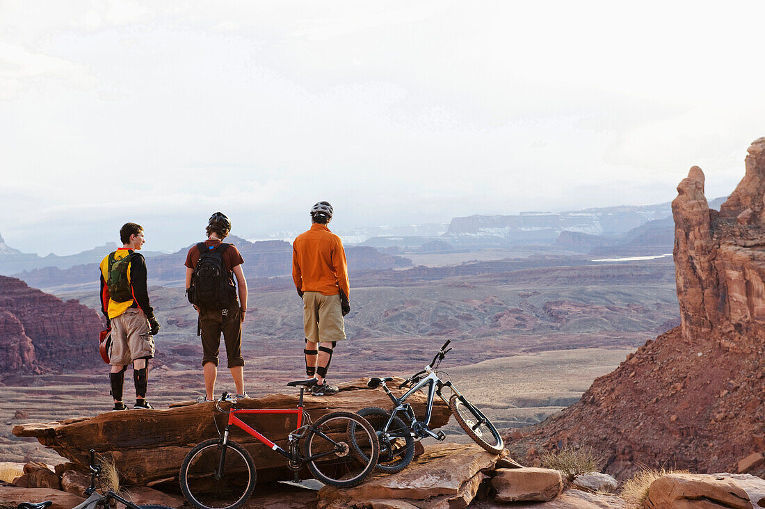 Three young men overlook a canyon after biking up the Amasa Back Trail, Moab, UT Moab, Utah, USA
