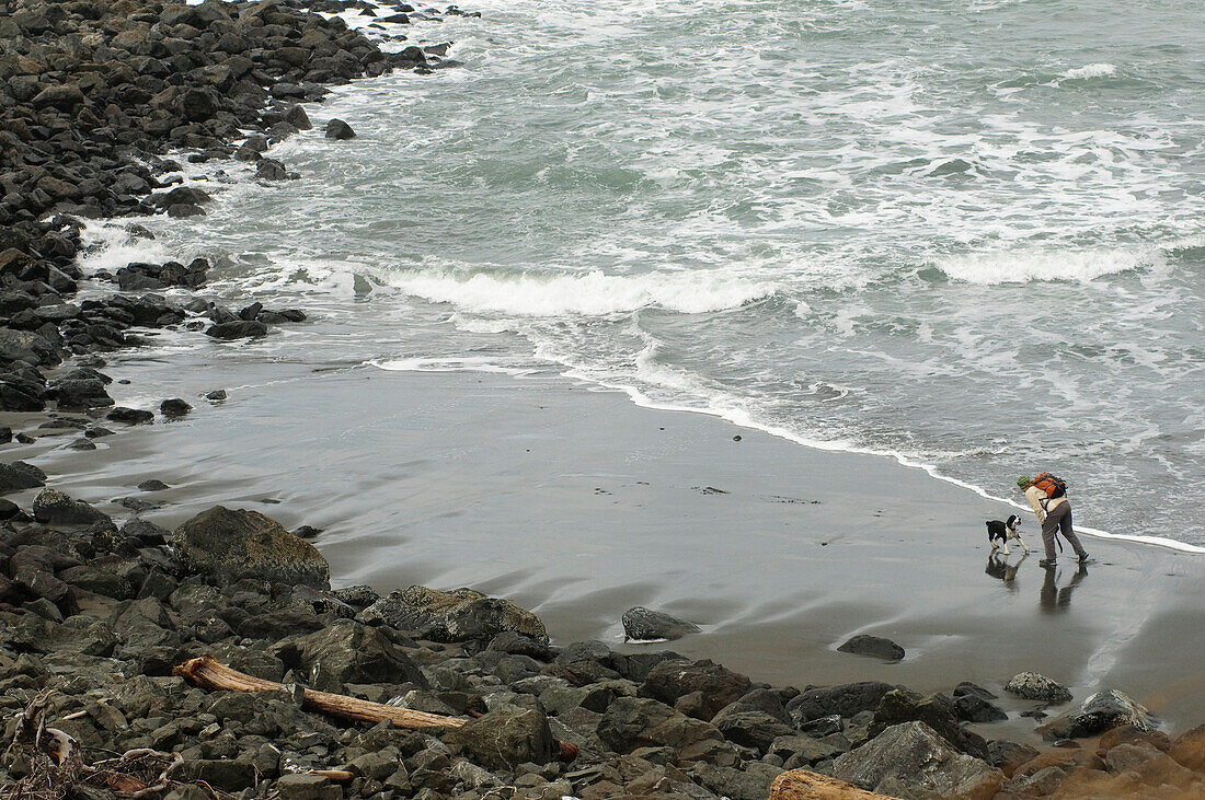 A woman hikes on a beach with her dog on the Oregon Coast Port Orford, Oregon, USA