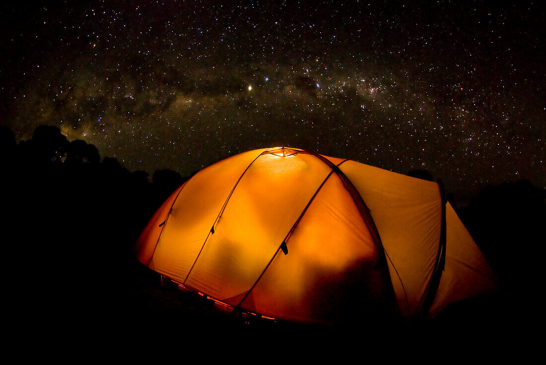 A tent illuminates the night as the Milky Way Galaxy floats above in a starry sky on Mt. Kilimnajaro Tanzania