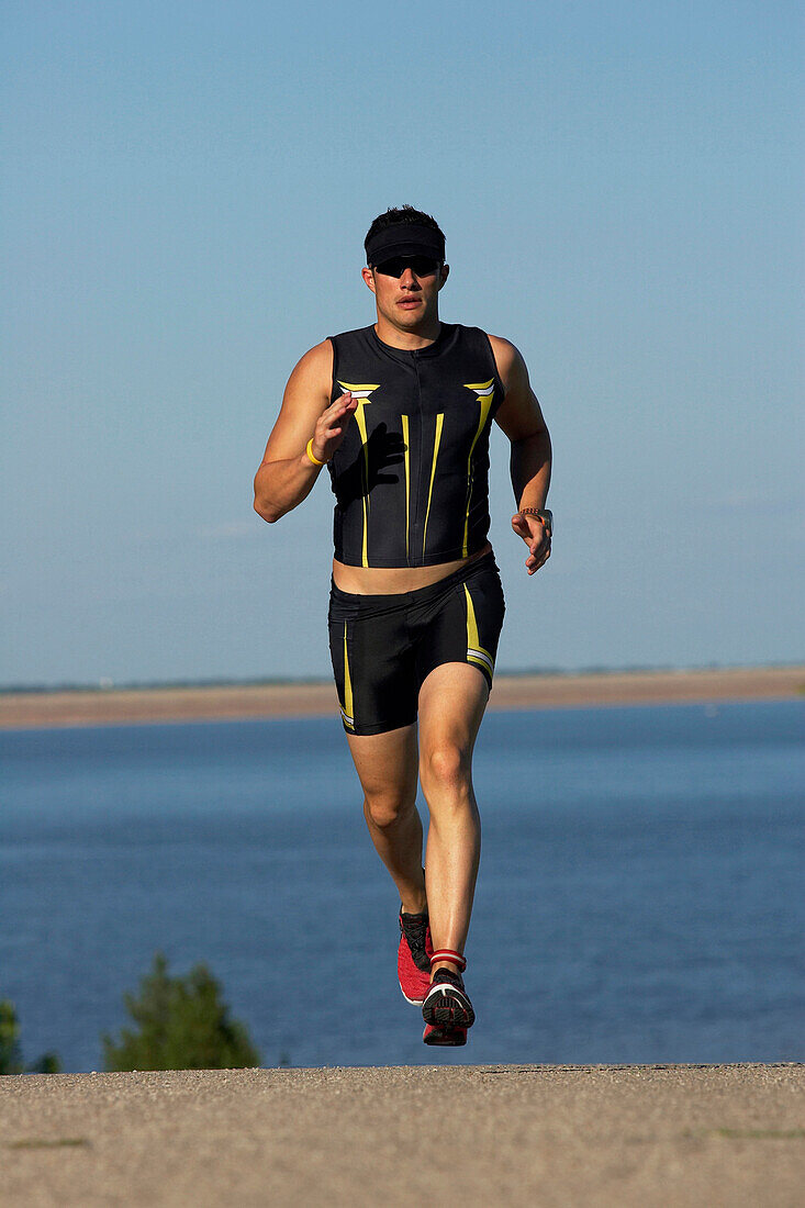 A male athelete running while training for a triathlon at a lake Lawrence, Kansas, USA