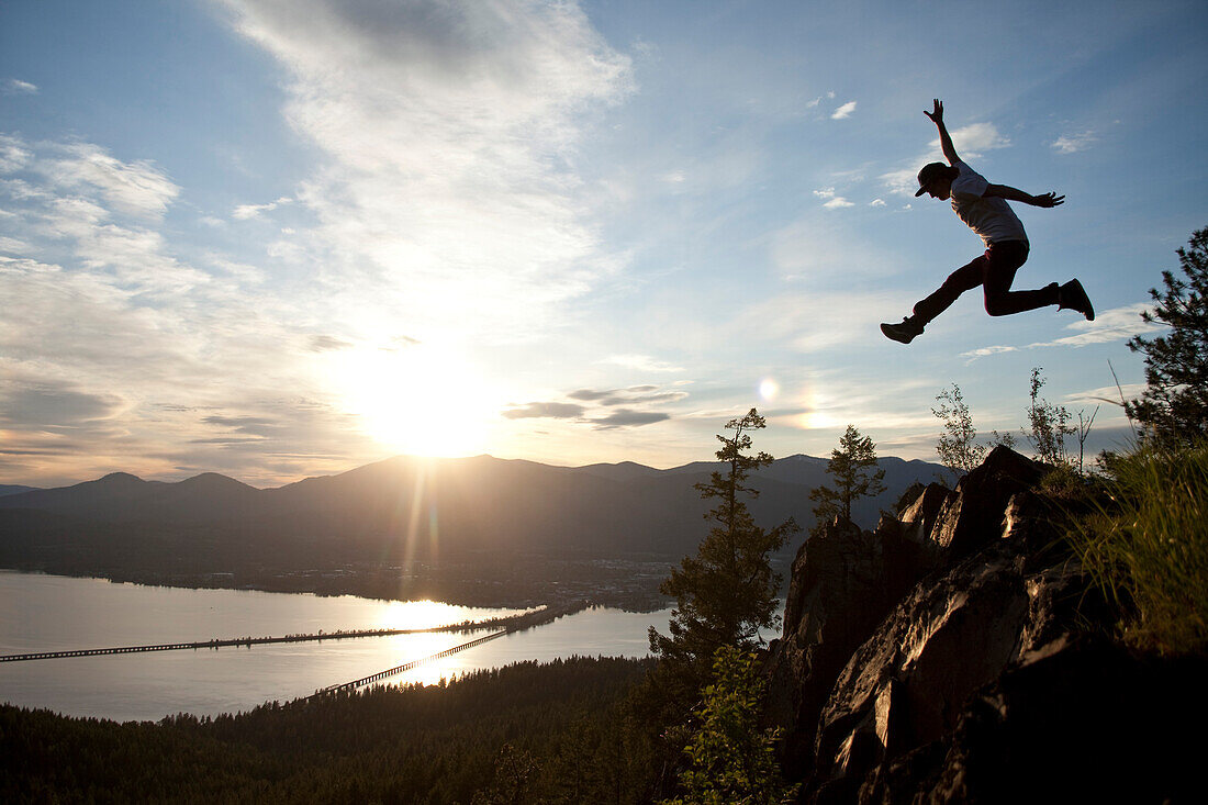 Young man soaring at sunset next to a large cliff overlooking  a lake Sandpoint, Idaho, USA