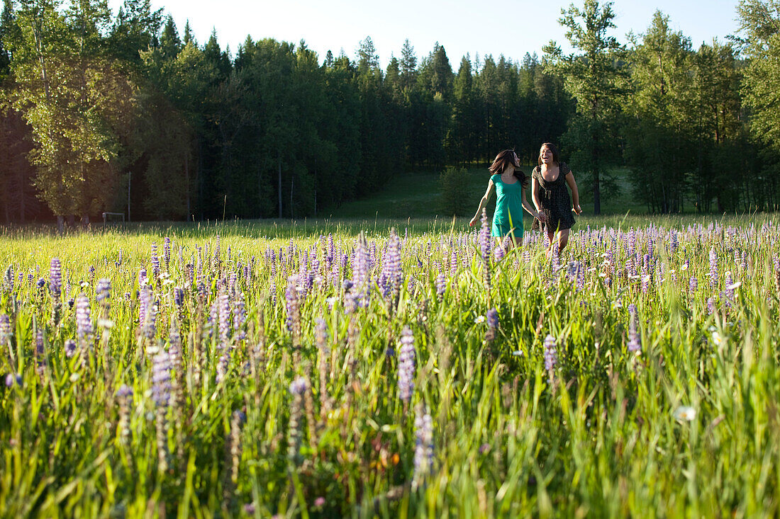 Two young women smile as they run through a field of wild flowers holding hands in Idaho Sandpoint, Idaho, USA