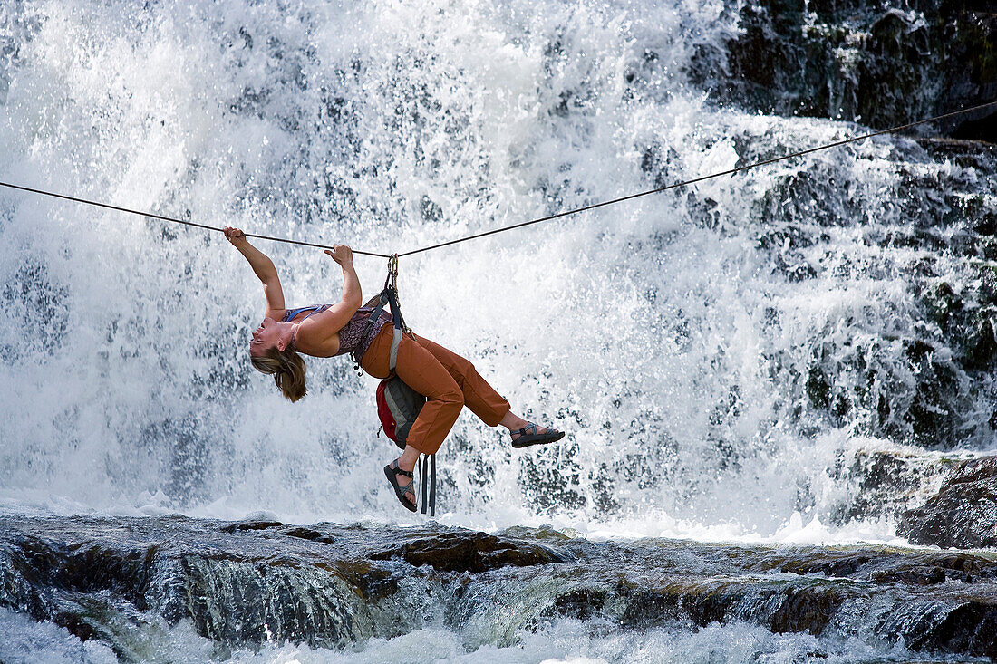 A woman crosses a waterfall using a Tyrolean Traverse on a rope Utah, USA