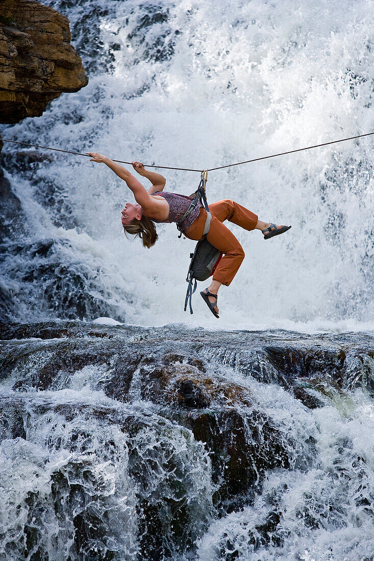 A woman crosses a waterfall using a Tyrolean Traverse on a rope Utah, USA