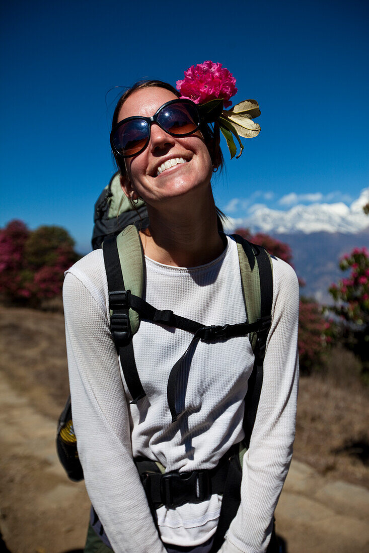 A female trekker wearing a flower in her hair stops to let the sun shine on her face Annapurna Conservation Area, Nepal