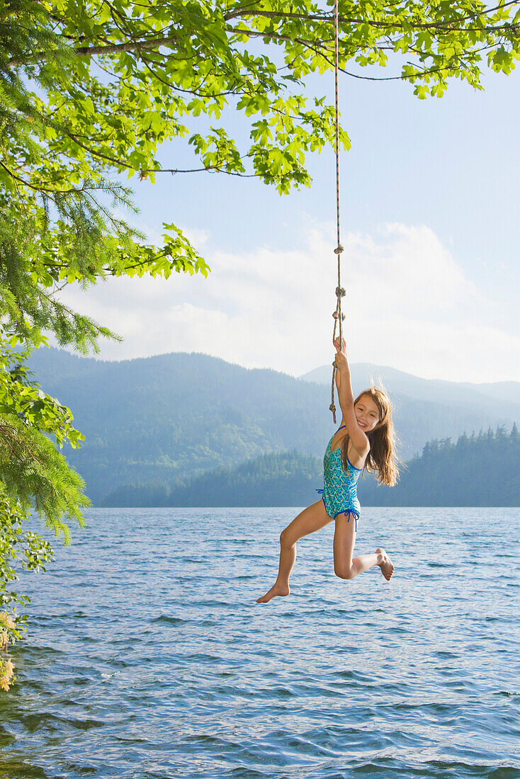Asian girl hanging from lake rope swing, Bellingham, WA