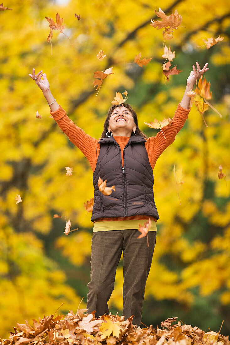 Hispanic woman throwing autumn leaves, Seattle, WA