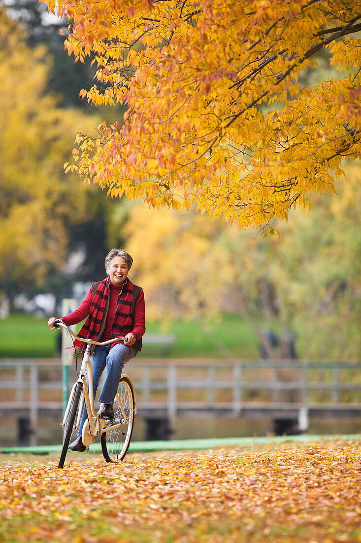 African woman riding bicycle in park in autumn, Seattle, WA