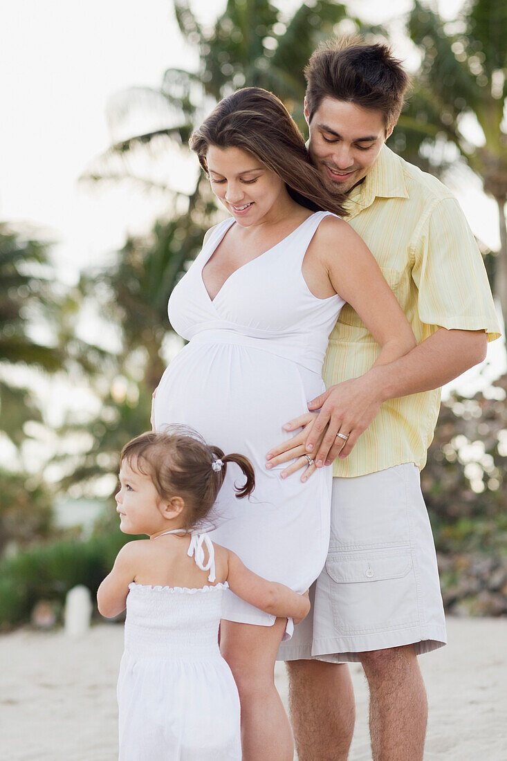 Husband hugging pregnant wife and watching daughter, Fort Lauderdale, FL