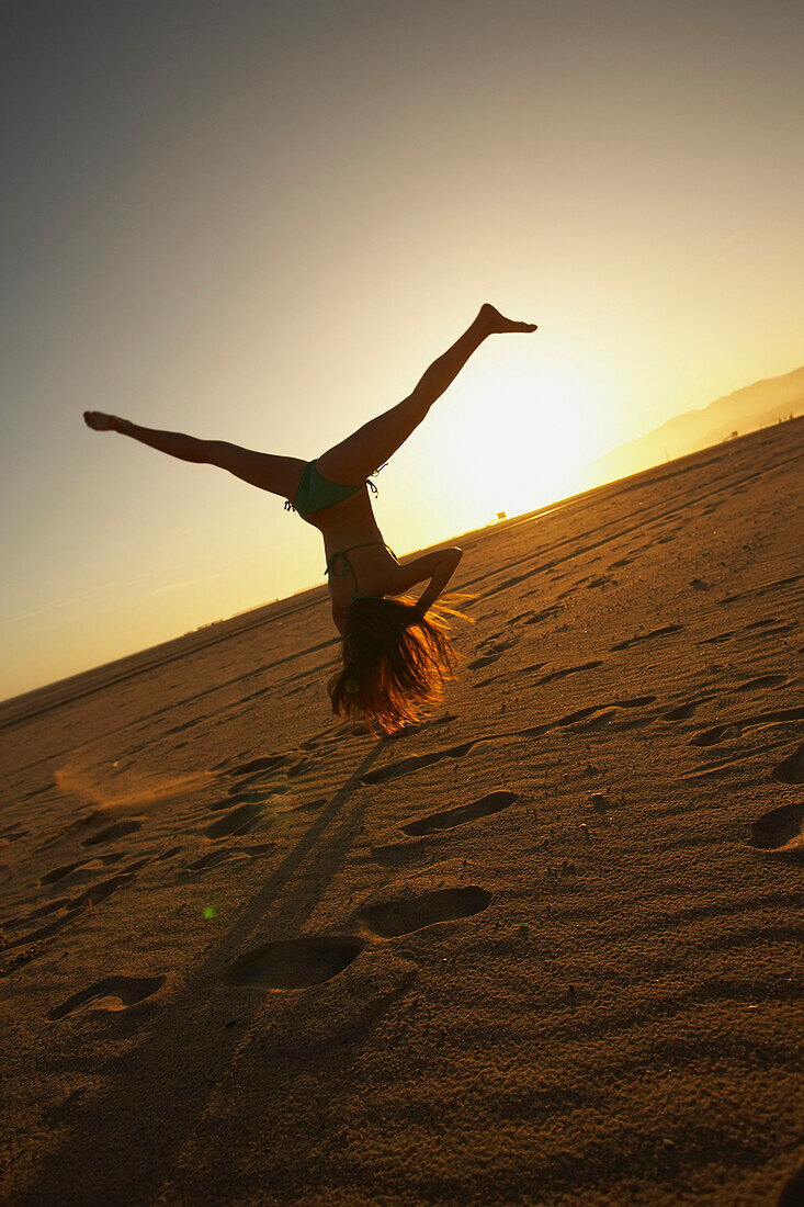 Mixed race woman doing cartwheel on beach, Santa Monica, CA