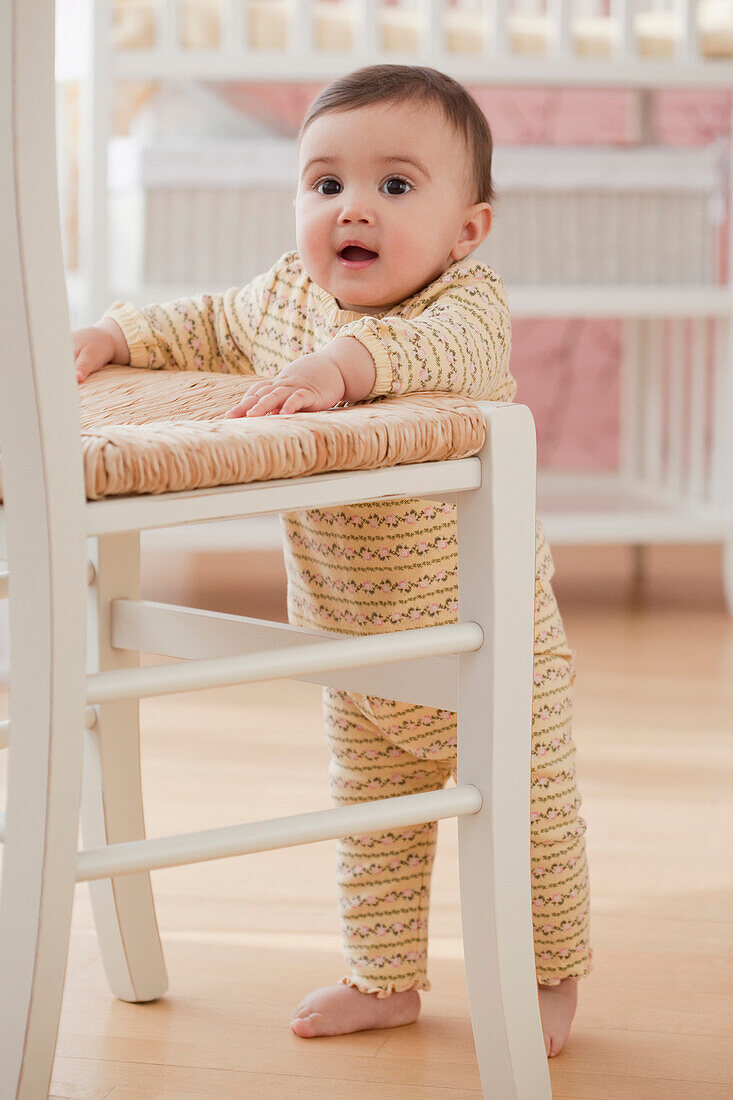 Mixed race baby girl balancing near chair, Jersey City, NJ