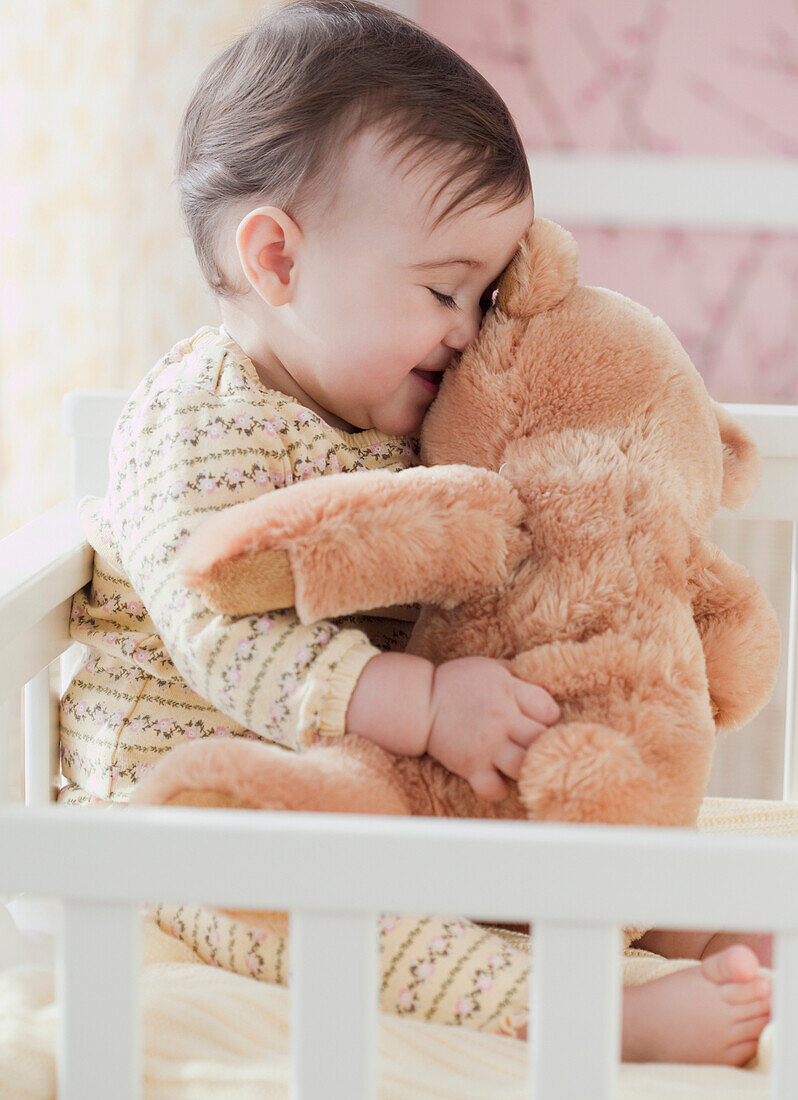 Mixed race baby girl snuggling teddy bear, Jersey City, NJ