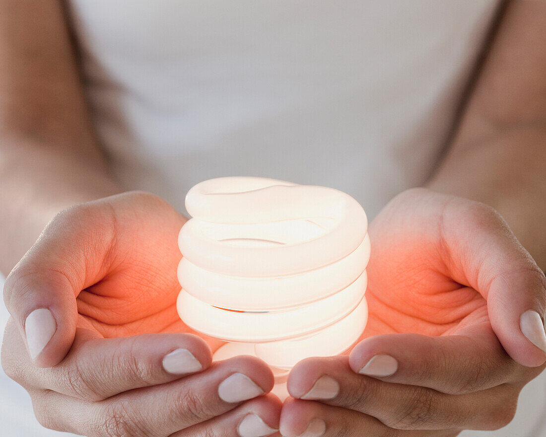 Woman holding glowing compact fluorescent bulb, Jersey City, NJ