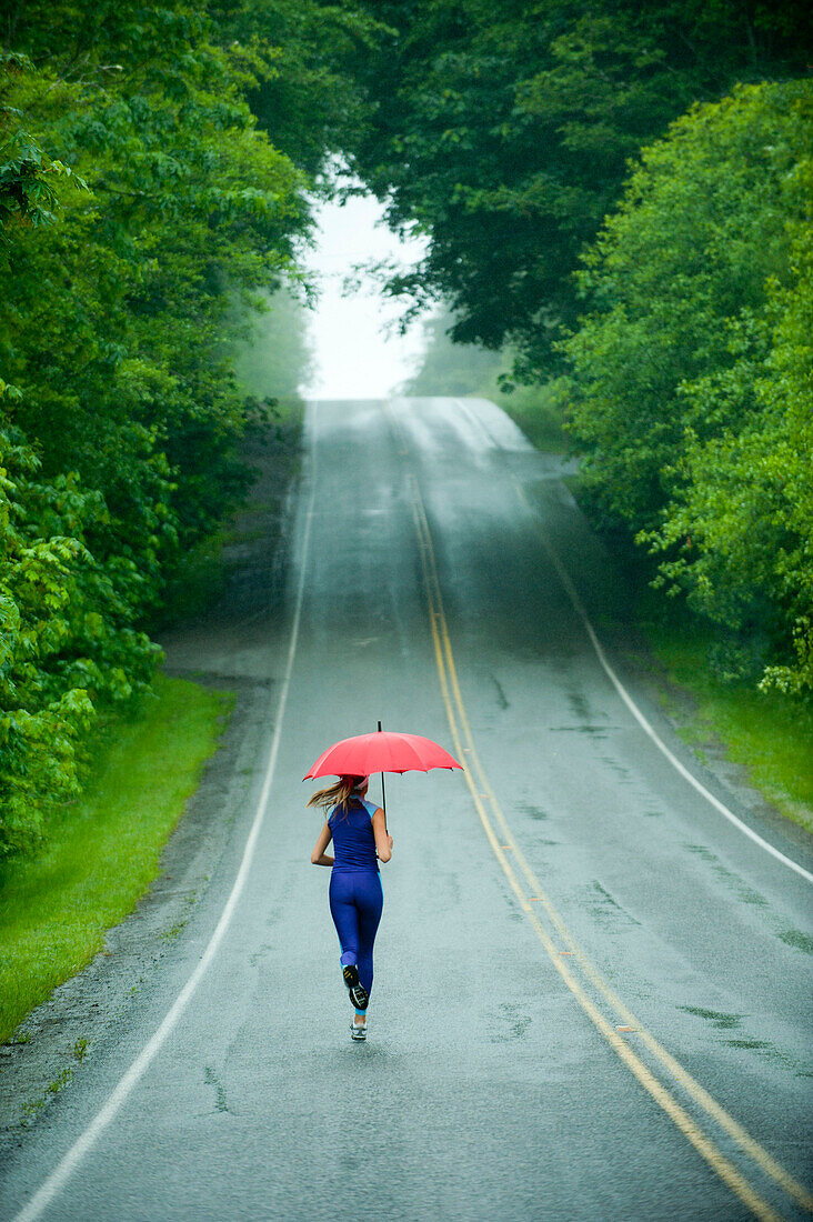 Caucasian woman running on remote road with umbrella, Bainbridge Island, Wa, USA