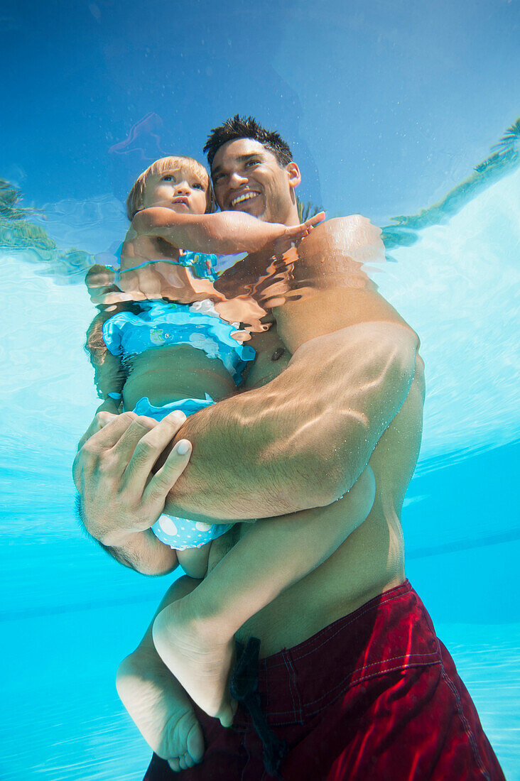 Mixed race father holding daughter in swimming pool, Ladera Ranch, CA, USA