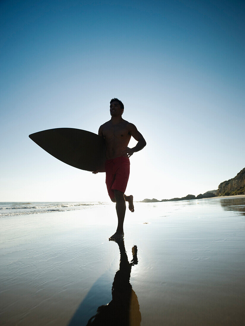Mixed race man carrying surfboard on beach, Newport Beach, CA, USA