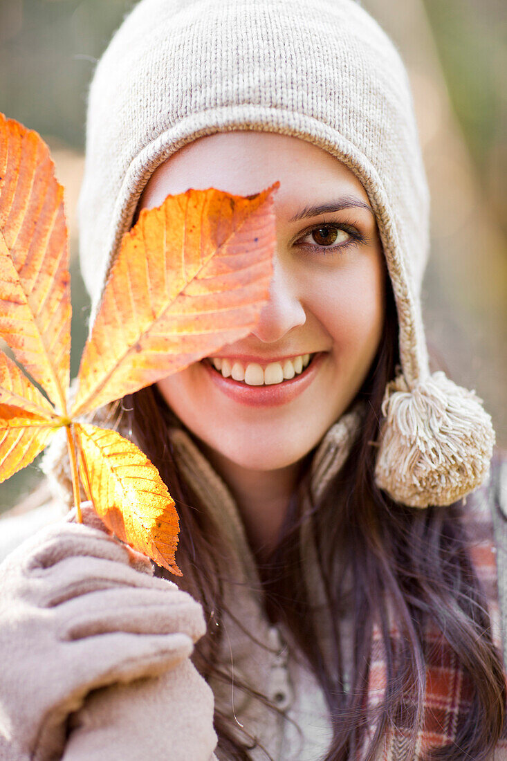 Mixed race woman in cap holding autumn leaf, Seattle, WA, USA