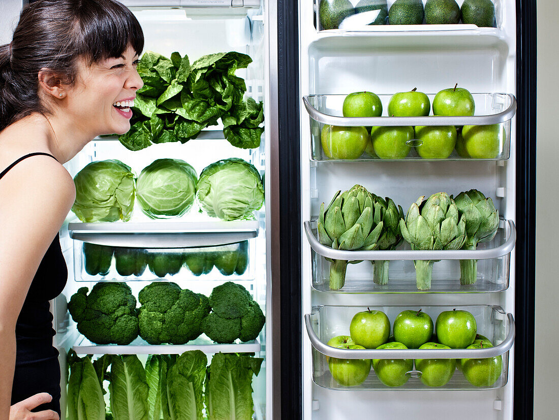 Gemischtrassige Frau betrachtet grünes Gemüse im Kühlschrank, Los Angeles, Kalifornien, USA