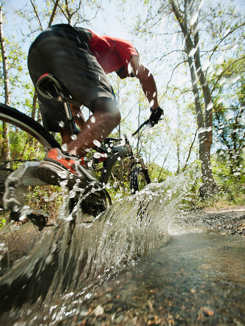 Mixed race man riding mountain bike through stream, Calabasas, California, United States