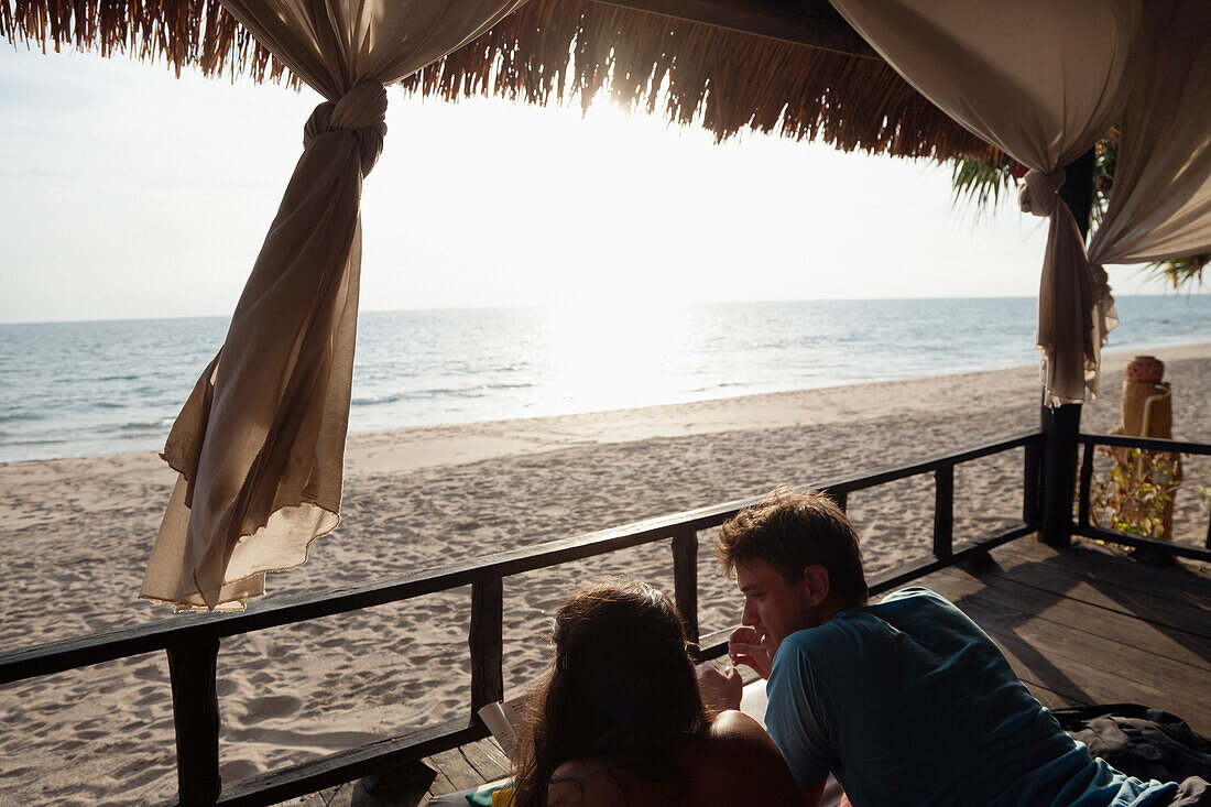 Couple laying on porch enjoying beach and ocean, Ko Lanta, Krabi, Thailand