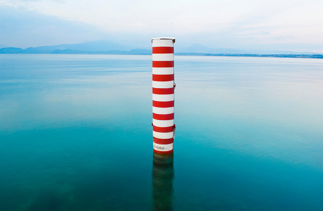 Red and white stripe pillar in tranquil lake, Lago Di Garda, Verona, United States