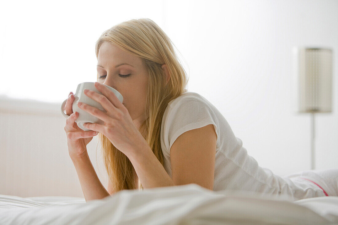 Caucasian woman laying in bed drinking coffee, Saint Louis, Missouri, United States