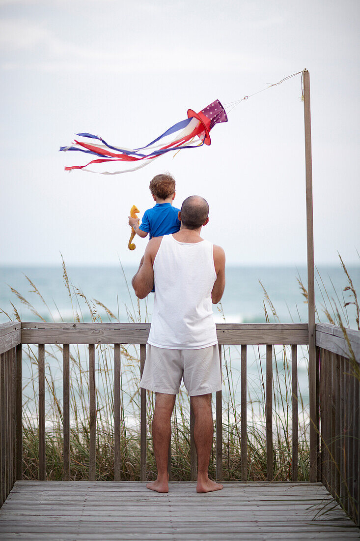 Father holding son on deck near ocean, Topsail Island, North Carolina, USA