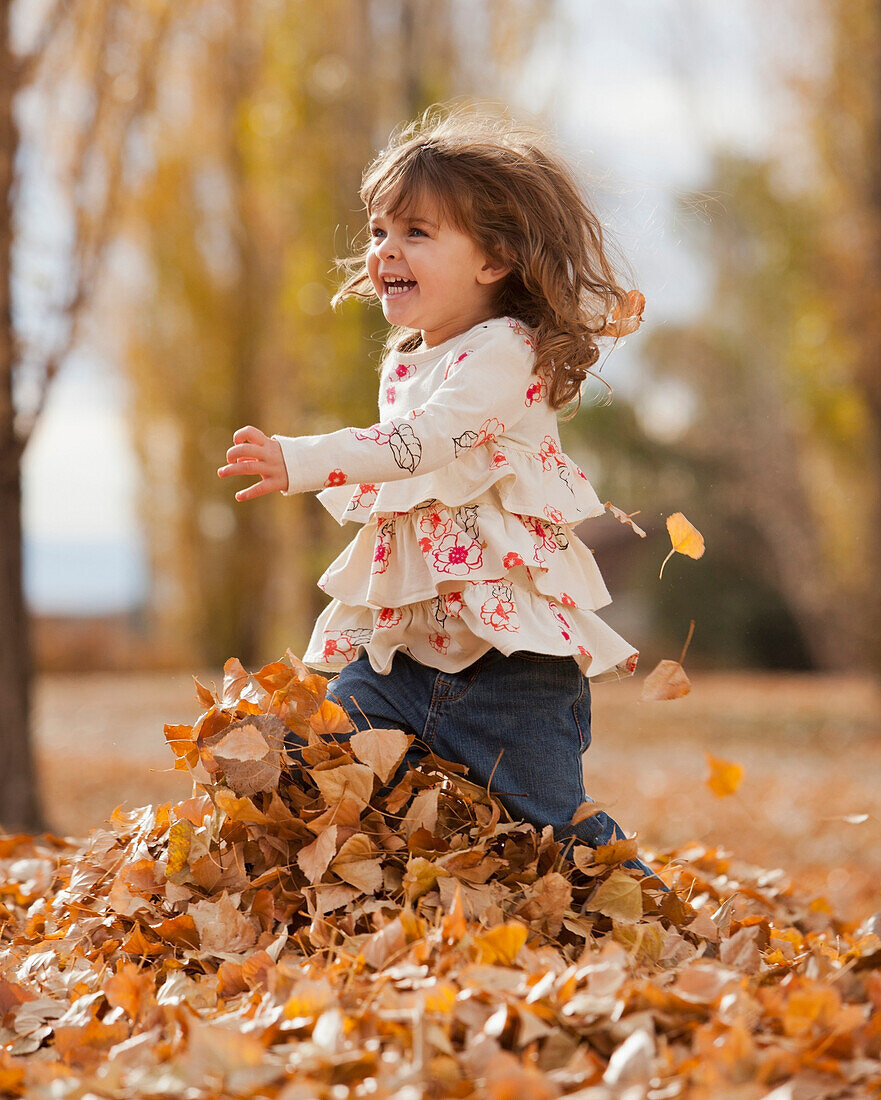 Caucasian girl playing in autumn leaves, Provo, Utah, USA