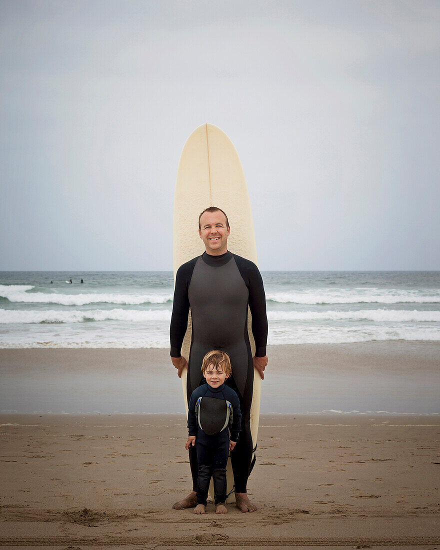 Caucasian father and son in wetsuits with surfboard, Manhattan Beach, California, USA