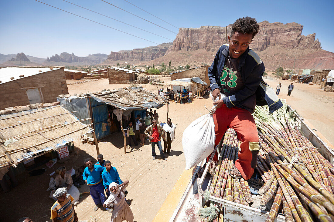 Zuckerrohr und Getreide wird auf das Dach eines Überlandbusses verladen, Gheralta Berge im Hintergrund, Magab, Tigray Region, Äthiopien