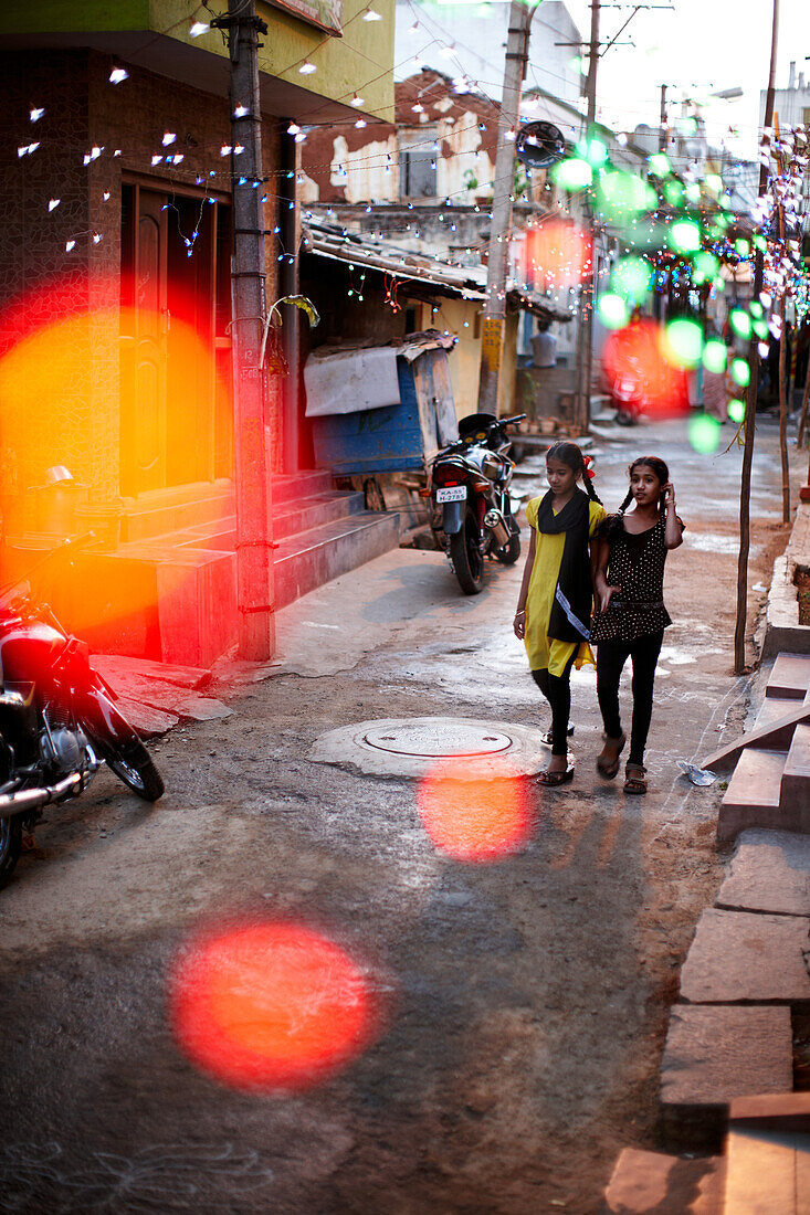 Mädchen laufen eine mit Lichterketten geschmückte Straße entlang, Mysore, Karnataka, Indien