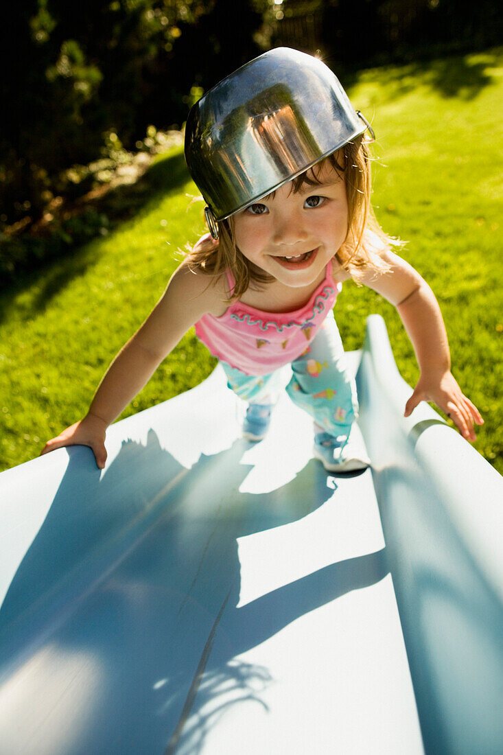 Portrait of girl climbing slide with bowl on head, Seattle, WA
