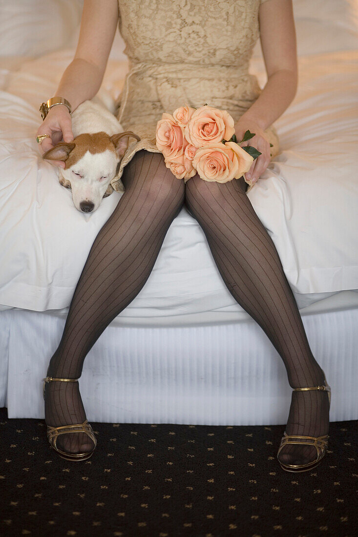 Woman in fancy dress with dog and flowers sitting on bed, Seattle, WA