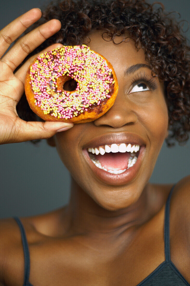 African woman holding doughnut over eye, Austin, TX