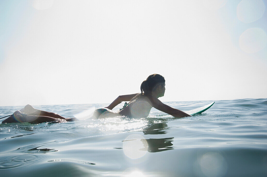Hispanic girl paddling on surfboard, Newport Beach, CA
