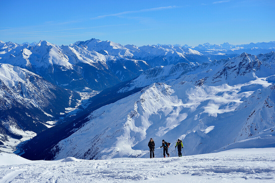 Three back-country skiers ascending to Agglsspitze, Zillertal Alps and the Dolomites in background, Agglsspitze, Pflersch Valley, Stubai Alps, South Tyrol, Italy
