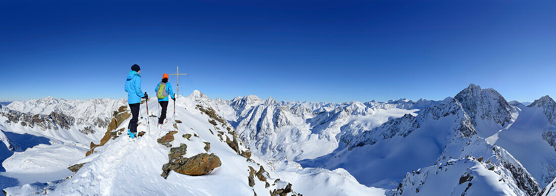 Two female back-country skiers beside Kuhscheibe summit cross, Stubai Alps, Tyrol, Austria