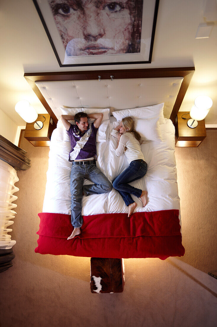 Paar liegt auf einem Doppelbett einer Suite, The Cambrian, Adelboden, Kanton Bern, Schweiz