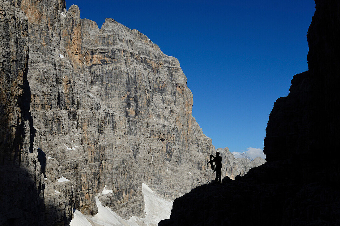 Kletterer präpariert Seil am Fuß des Campanile Basso, Crozzon di Brenta im Hintergrund, Trentino, Italien