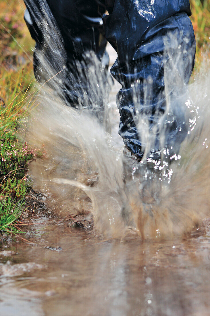 Wanderer in Regenkleidung läuft durch Wasser, Letterewe Wilderness, Highlands, Schottland, Großbritannien