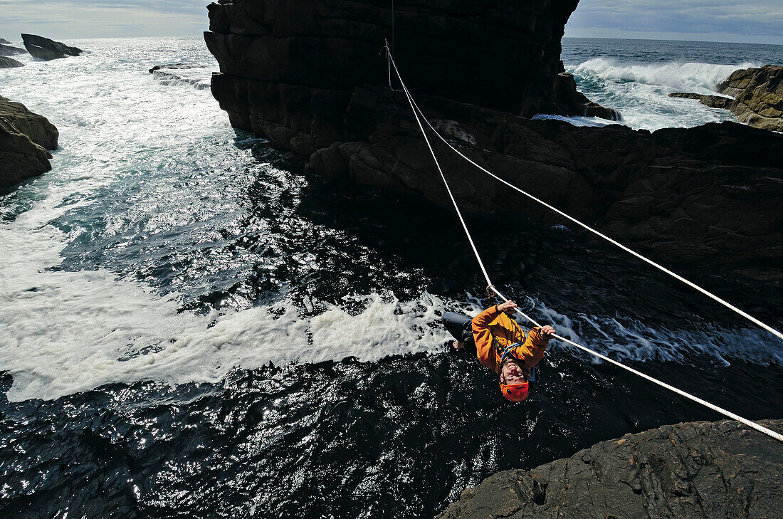Man climbing along rope to Old Man of Stoer, Stoer, Highlands, Scotland, Great Britain