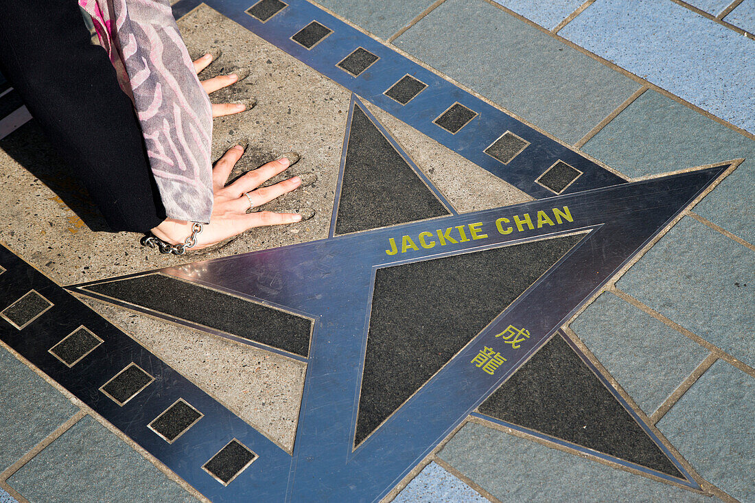 Woman placing her hands in the handprints of film star Jackie Chan on the Avenue of Stars promenade along Hong Kong Harbour waterfront, Tsim Sha Tsui, Kowloon, Hong Kong