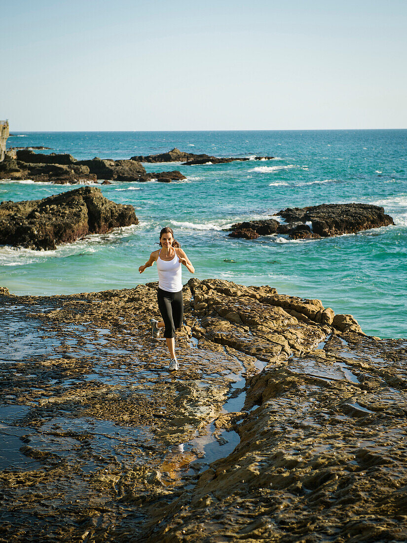 Mixed race woman running on rocky beach, Laguna Beach, California, USA