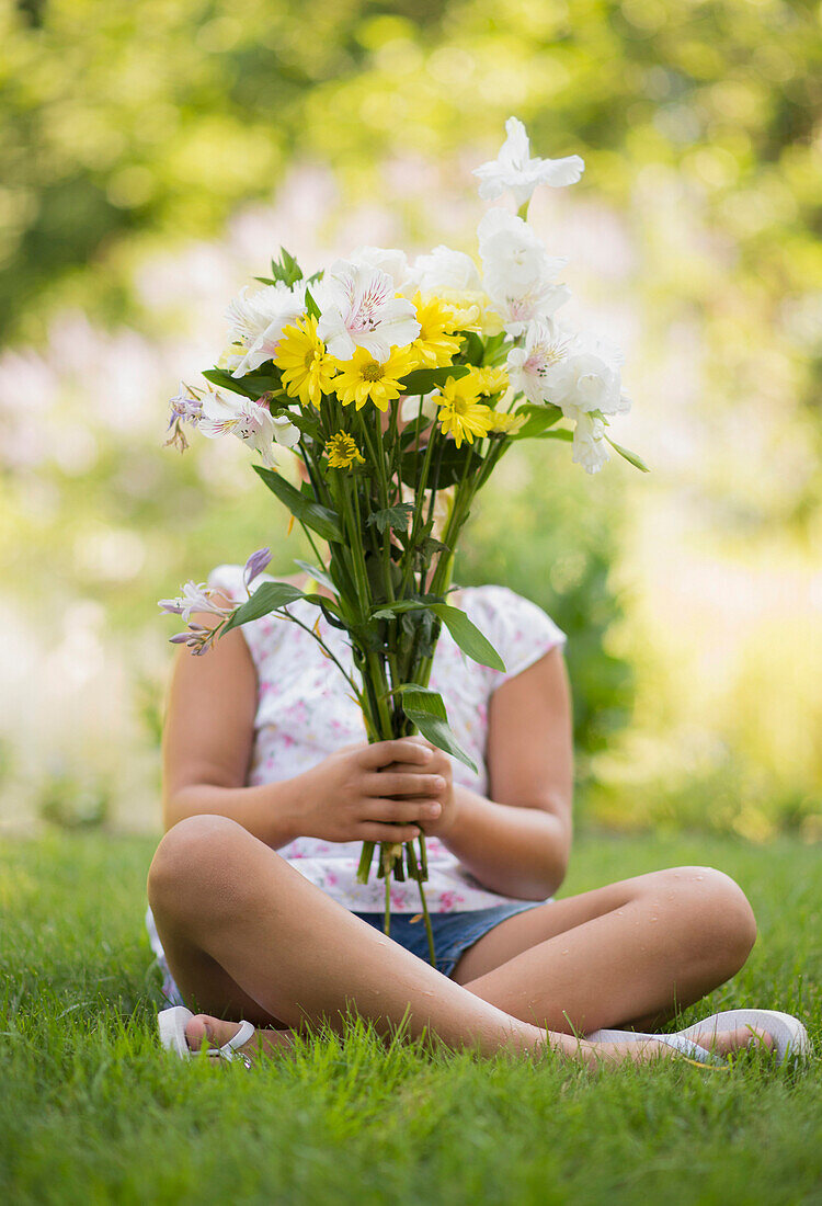 Mixed race girl holding bouquet of flowers in grass, Huntington Station, New York, USA