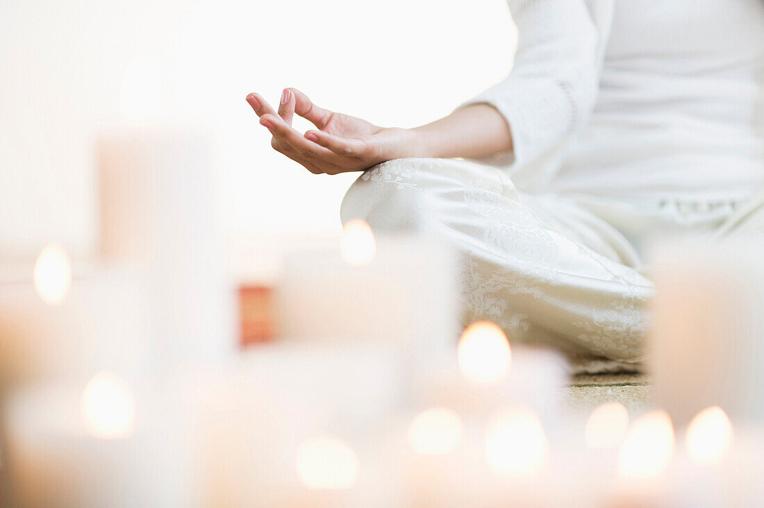 Hispanic woman meditating in lotus position near lit candles, Jersey City, NJ, USA