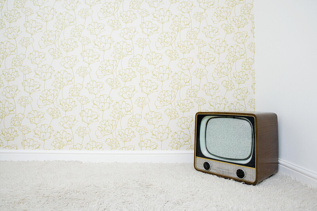 Retro television in corner of room with patterned wallpaper