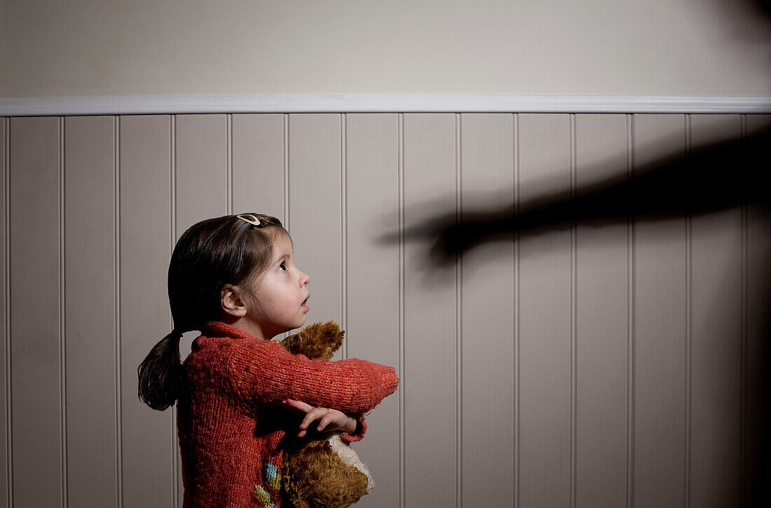 Frightened little girl and shadow of adult hand pointing at her