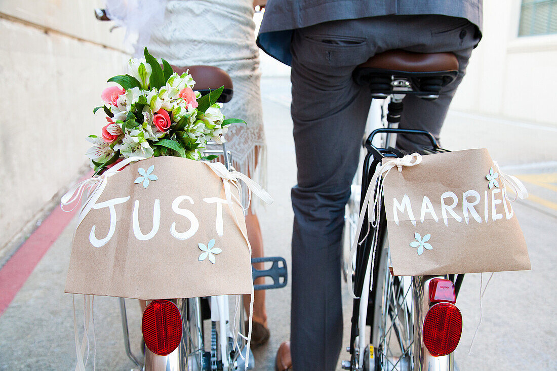 Young newlywed couple cycling along street, rear view, close up