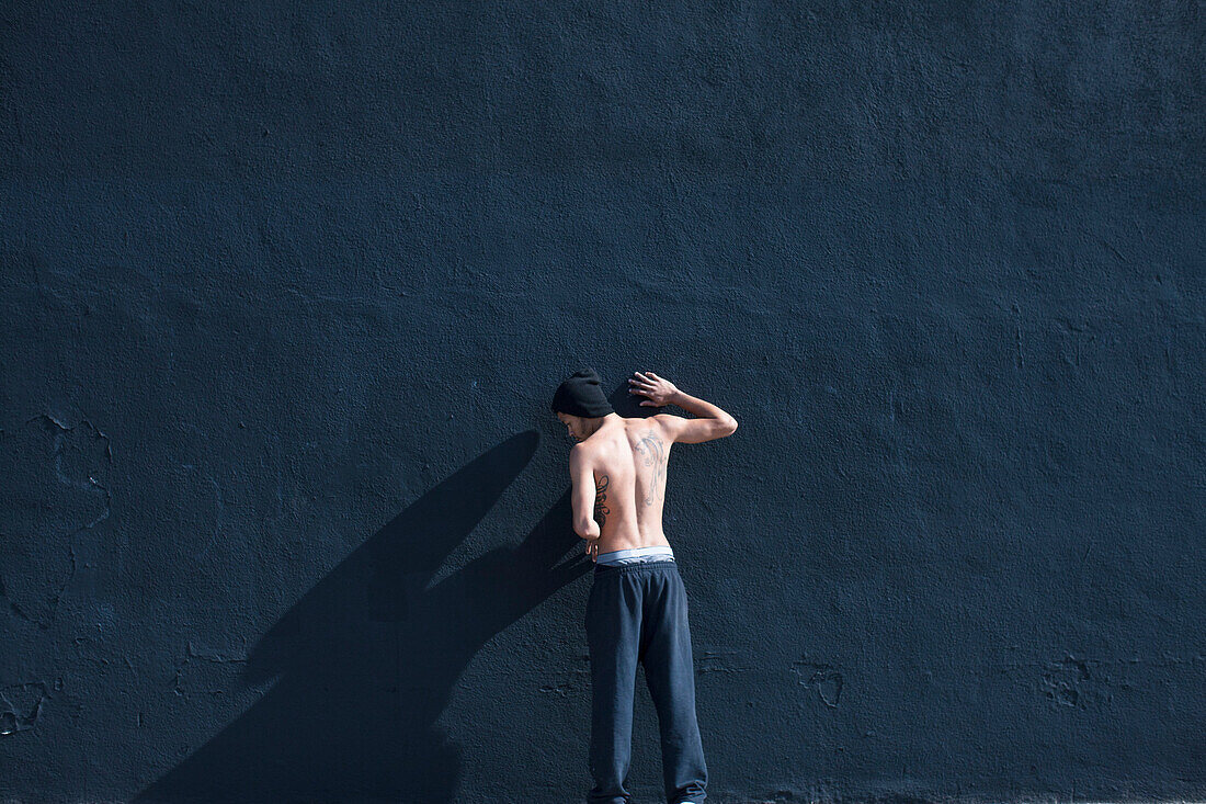 Barchested man leaning against a wall
